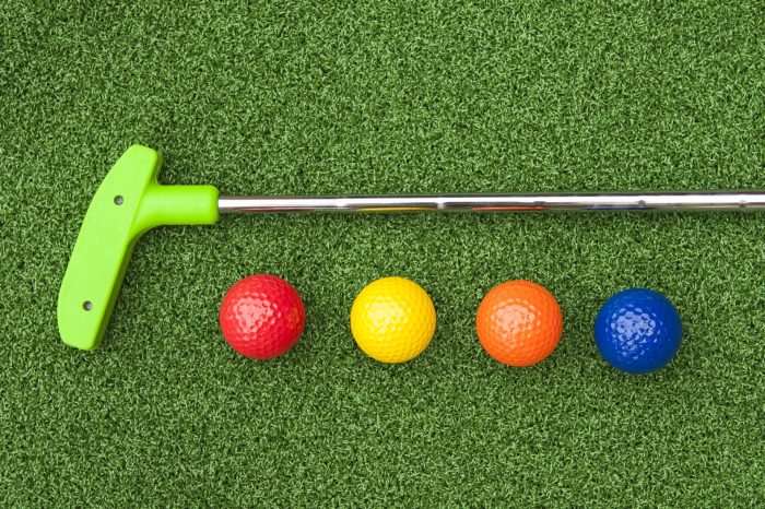 Green putter with golf balls on artificial grass